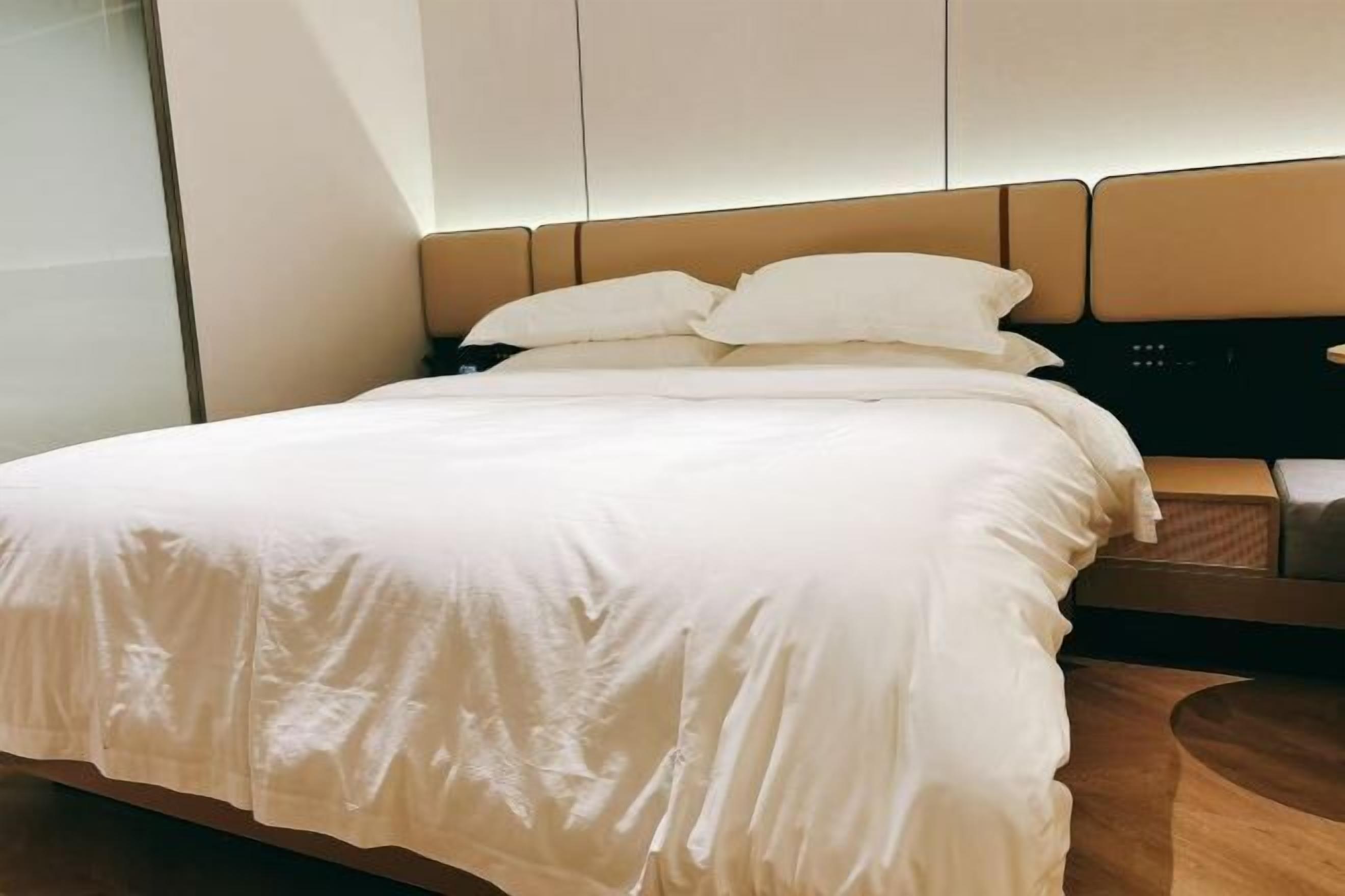 Una cama bien hecha con cabecera, una mesita de noche y un panel de control en la pared.