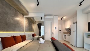 Une chambre d’hôtel moderne dotée d’un grand lit, d’une banquette, d’une kitchenette et d’une salle de bain visible à travers une porte en verre.