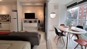 Un salon moderne comprenant un coin repas, un téléviseur à écran plat et une grande fenêtre donnant sur la ville.