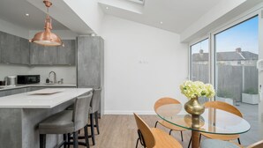 A modern kitchen with a large island, a dining area with a glass table, and a view of the outside. - Elegant 3Bedroom Retreat (London)