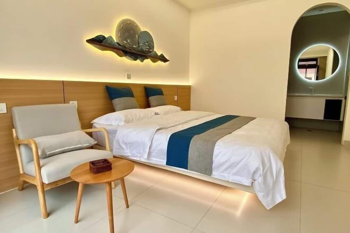 Quarto de hotel moderno com cama, uma cadeira, uma mesa pequena, um elemento decorativo na parede e um espelho.