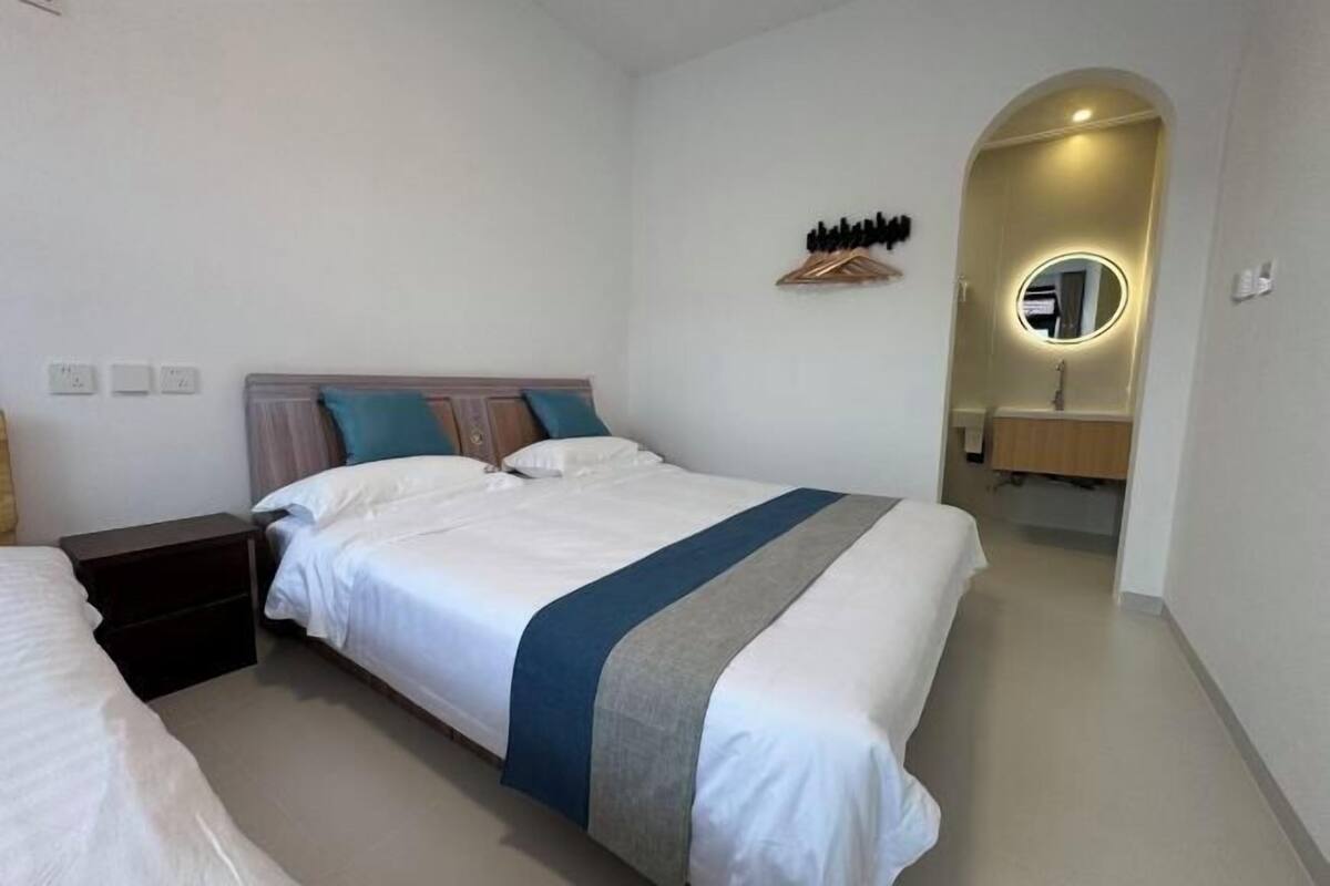Quarto de hotel com uma cama grande, uma mesa de cabeceira, um espelho e um banheiro pequeno com pia.