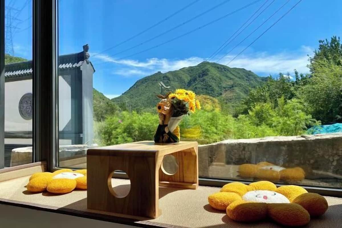 Vista de uma montanha através de uma janela, com um banquinho de madeira e brinquedos macios no parapeito.