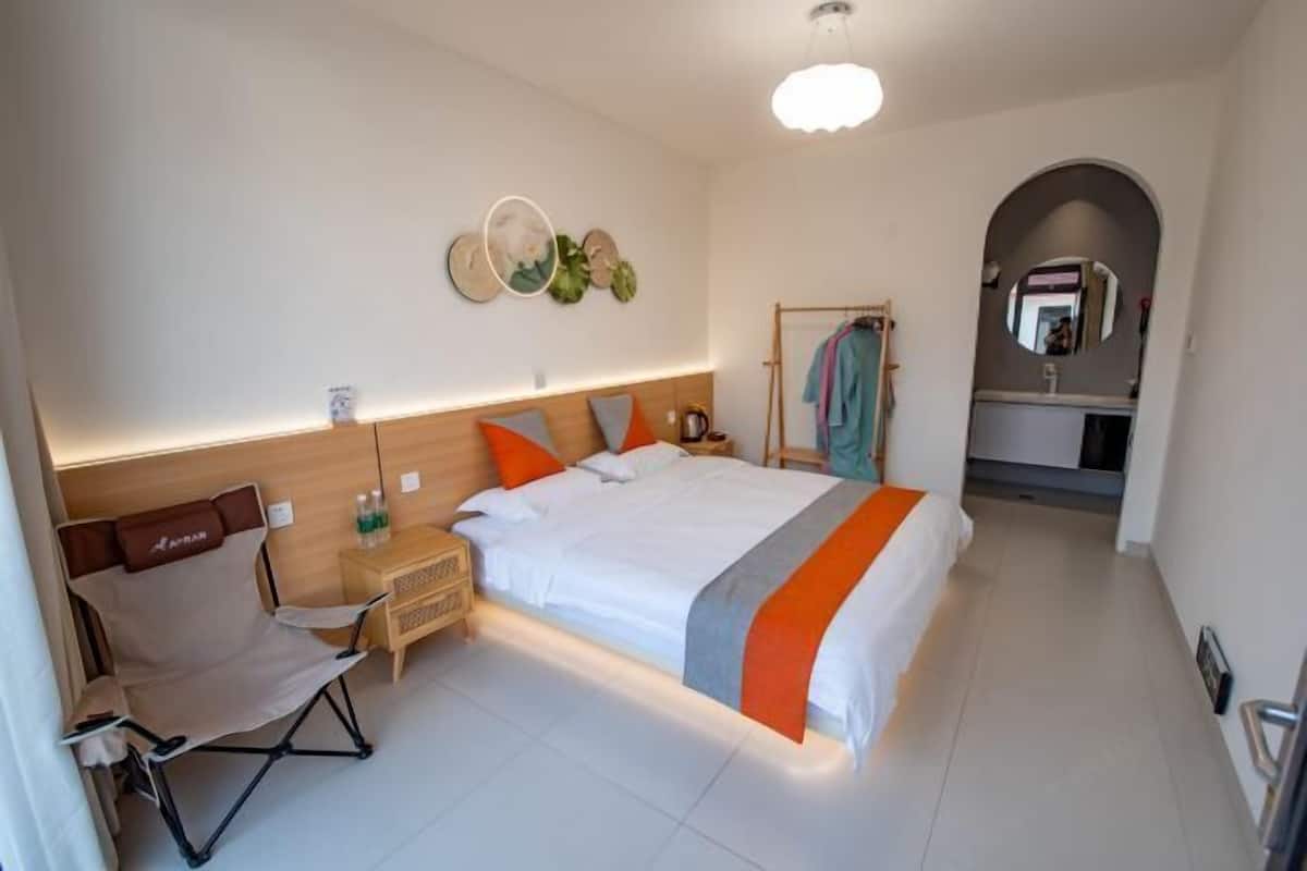Quarto de hotel com cama, cadeira, mesa de cabeceira, espelho e uma pequena área de kitchenette.