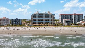 Un hôtel situé en bord de mer, composé de plusieurs bâtiments, avec une plage de sable et des vagues de l’océan.