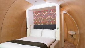 Une chambre à coucher comprenant un lit, une tête de lit, un mur orné d’un motif floral, une table de chevet et une petite salle de bain avec un lavabo.