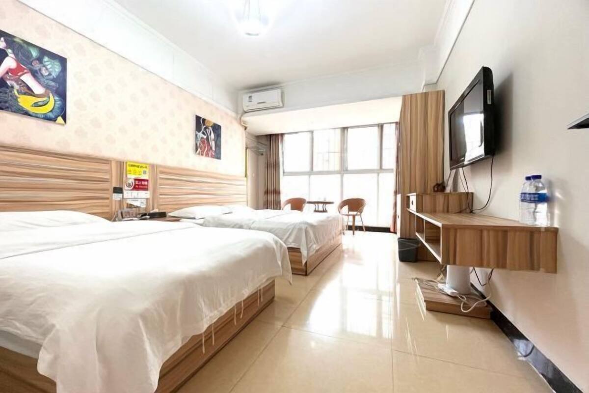 A hotel room with two beds, a TV, a wooden shelf, and a window with a view.