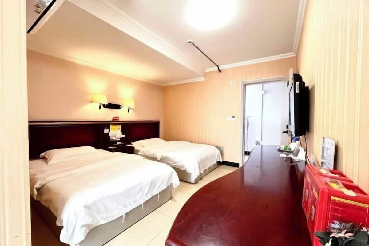 A hotel room with two beds, a wooden headboard, a flat-screen TV, a desk with a chair, and a red storage unit.