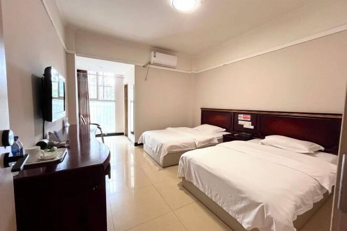 A hotel room with two beds, a desk with a chair, a television, and an air conditioning unit.