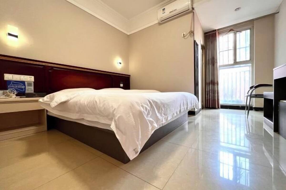 A hotel room with a bed, a desk, an air conditioning unit, and a window with curtains.