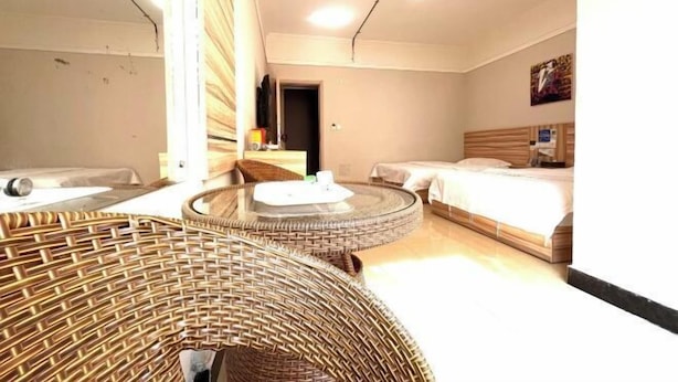 Una habitación de hotel con una cama, una silla redonda de mimbre, una mesita pequeña y un espejo.