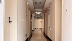 Un pasillo largo y estrecho con paredes color beige y un piso brillante, que conduce a una puerta al final.