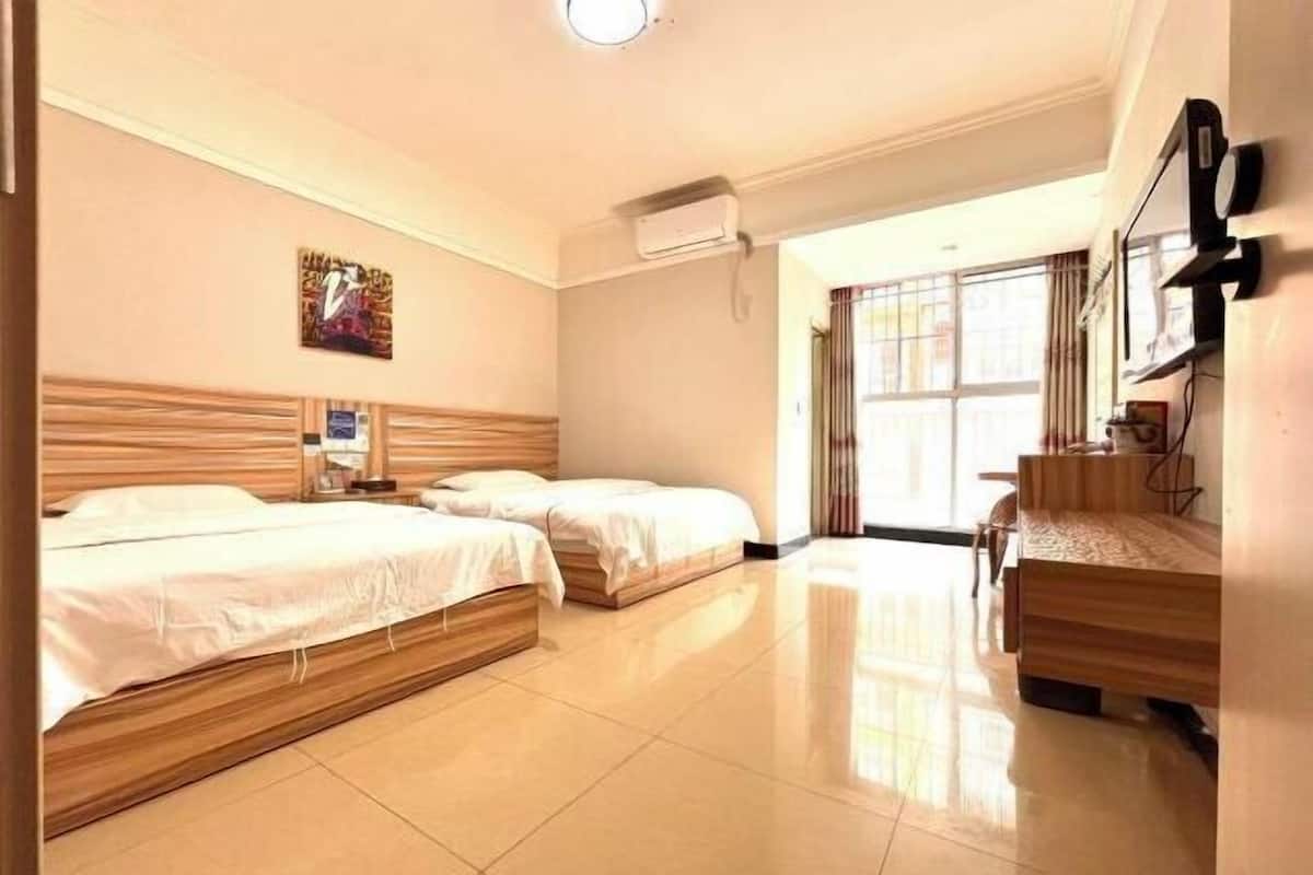 A hotel room with two beds, a desk, a chair, a TV, and an air conditioning unit.