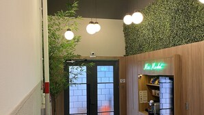 A hallway with a reception desk, a green cushioned bench, and a wall with a green leafy wall. - Zest Teodoro (São Paulo)