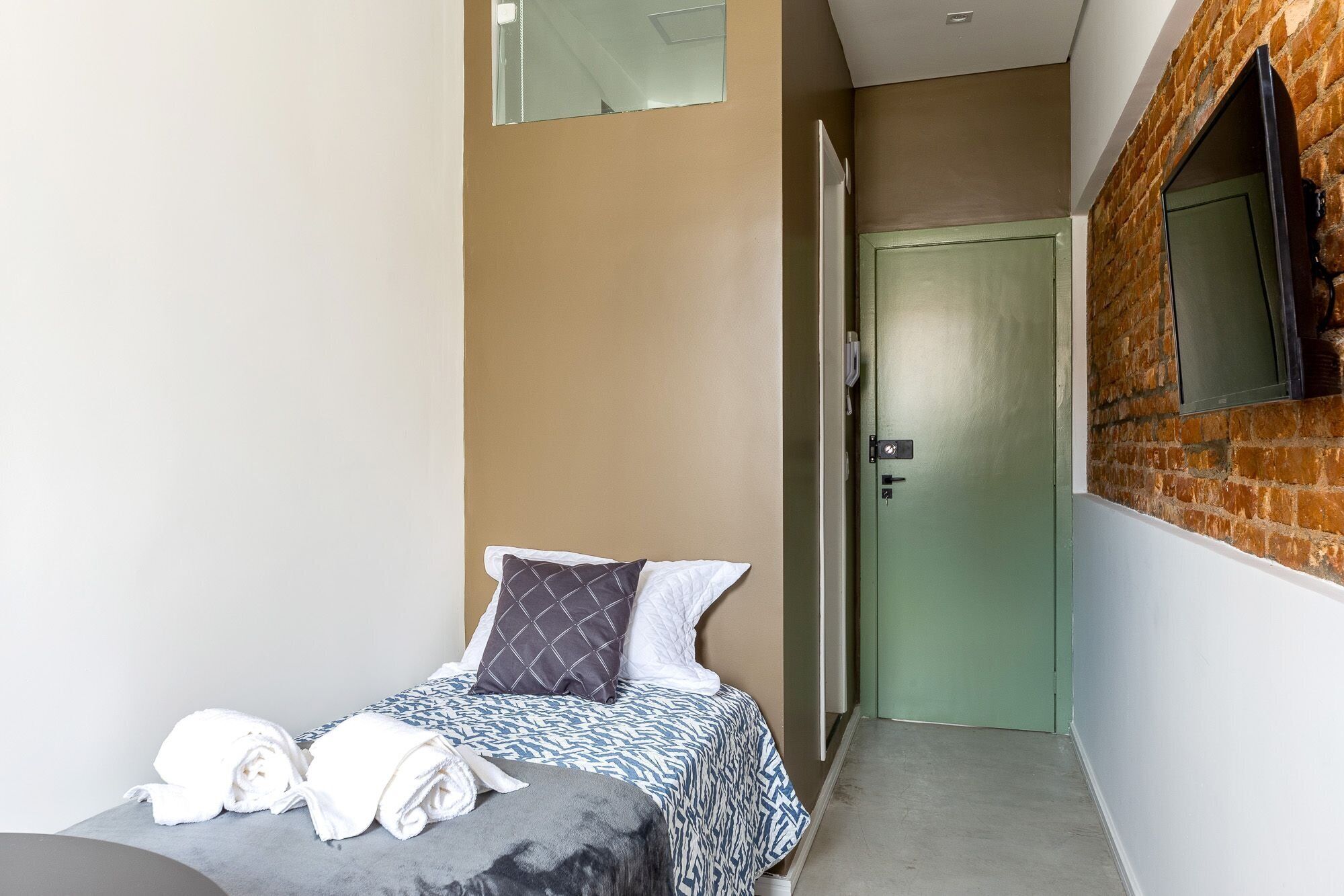 A bedroom with a bed, a towel, a pillow, a door, and a brick wall.