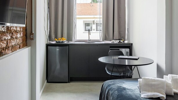 A compact hotel room with a kitchenette, a bed, a TV, and a window with curtains. - Zest Teodoro (São Paulo)