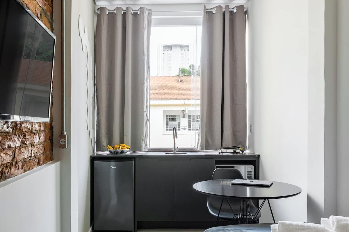 A compact hotel room with a kitchenette, a bed, a TV, and a window with curtains.