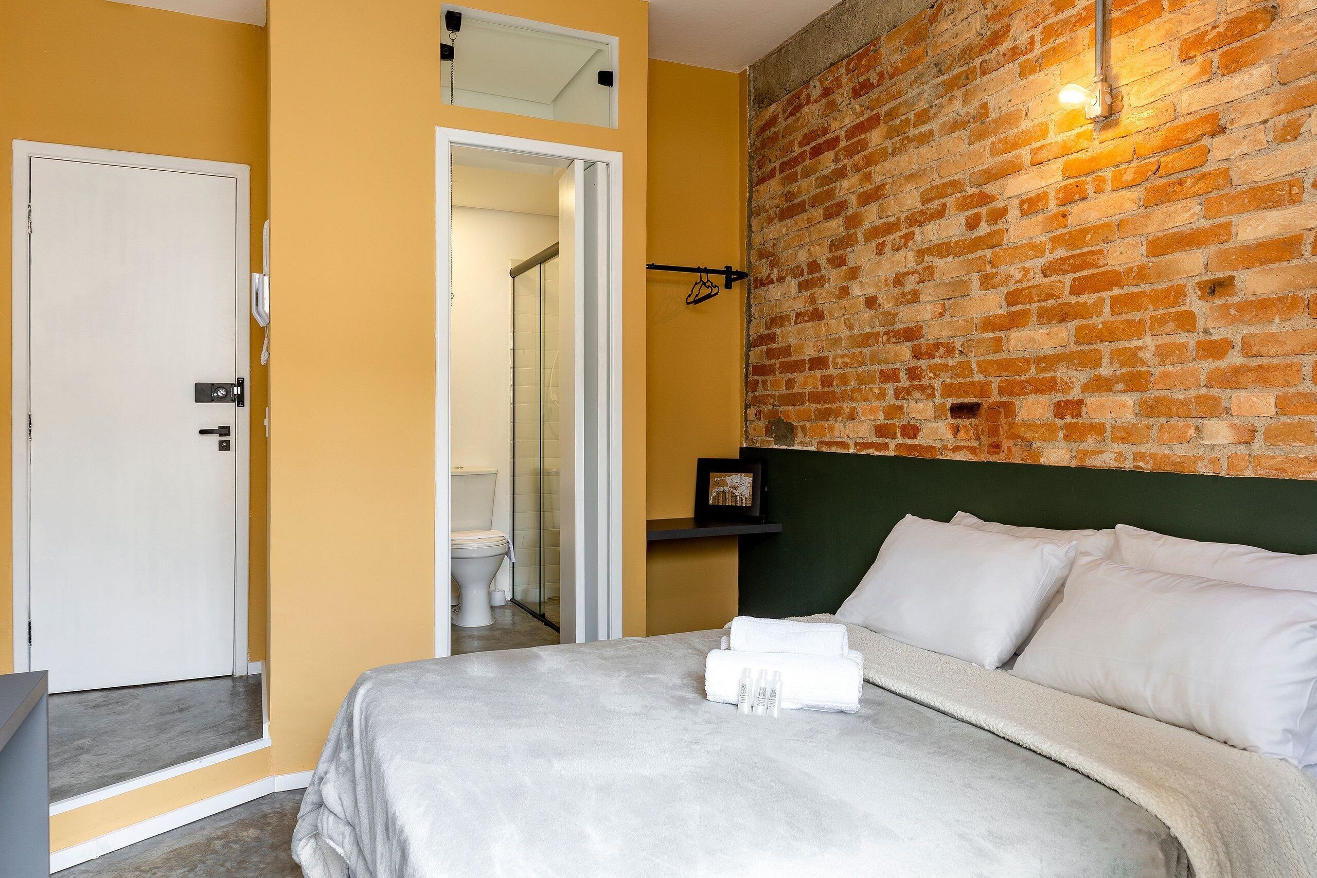 Una habitación de hotel con una cama, baño y pared de ladrillo.