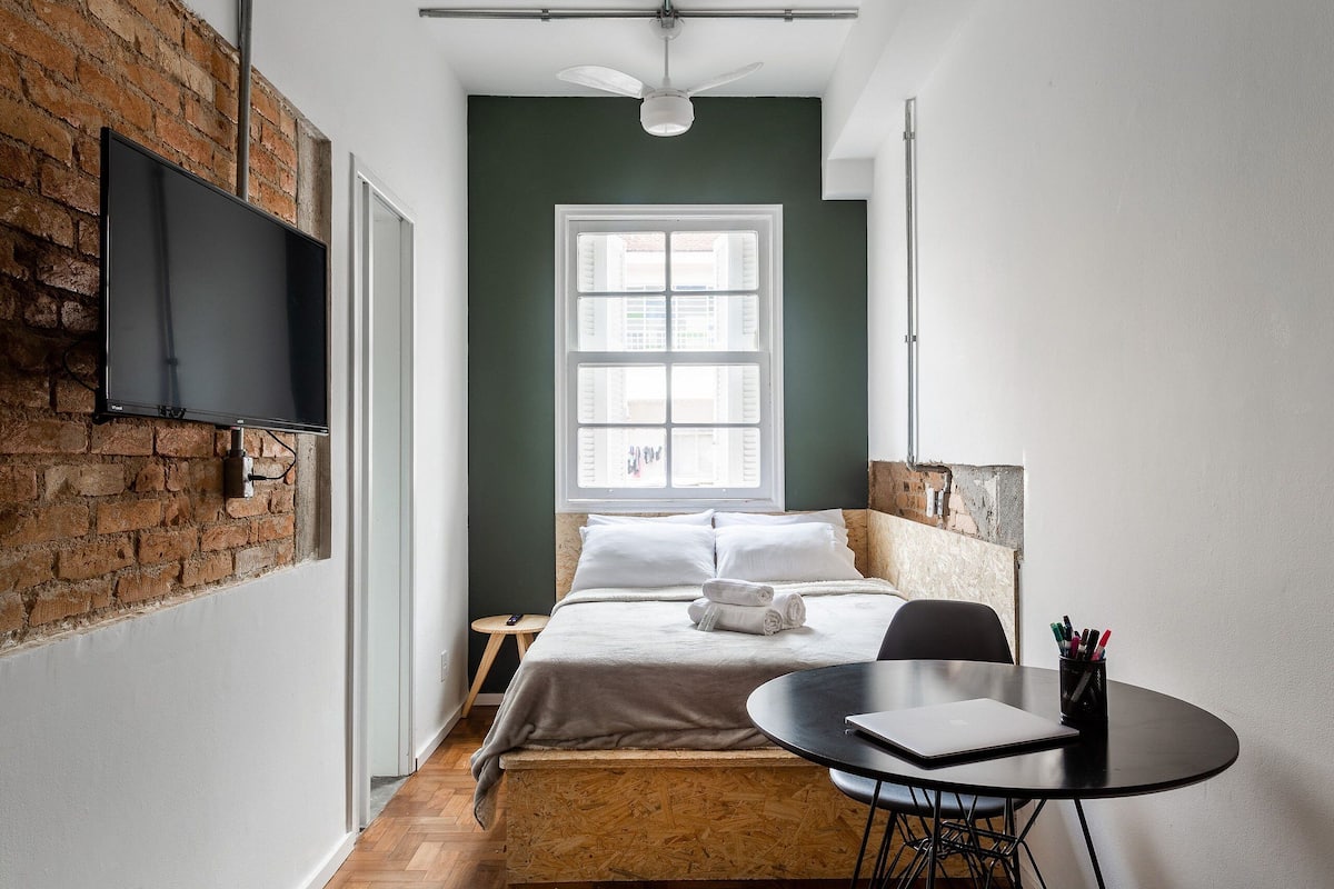 A room with a bed, a desk, a chair, a TV, and a window.