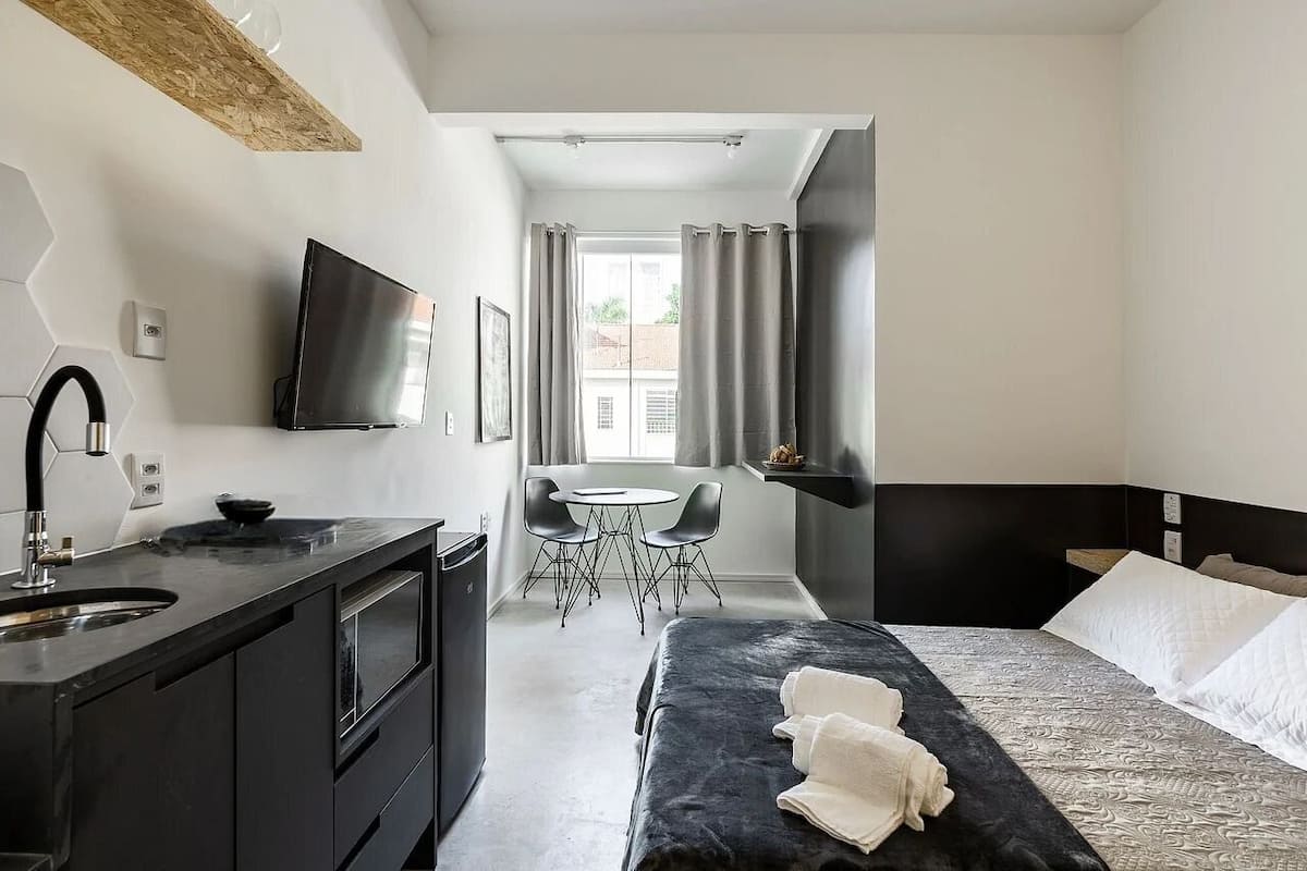 A modern hotel room with a bed, a desk, a sink, and a TV.