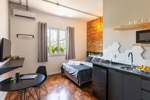 A compact hotel room with a bed, a desk, a kitchenette, and a window with curtains. - Zest Teodoro (São Paulo)