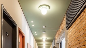 A hallway with wooden flooring, doors numbered 210 and 301, and a brick wall on one side. - Zest Teodoro (São Paulo)