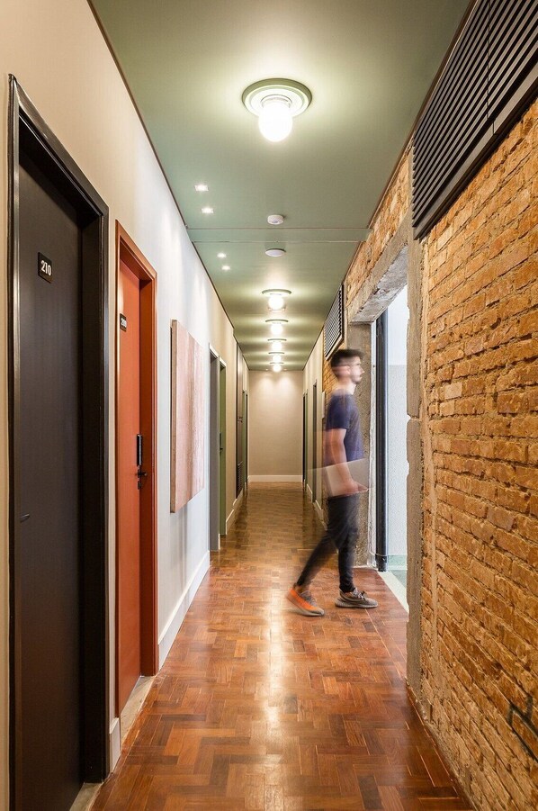 A hallway with wooden flooring, doors numbered 210 and 301, and a brick wall on one side. - Zest Teodoro (São Paulo)