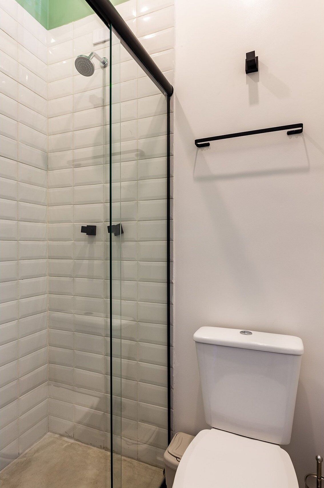 A bathroom with a glass shower enclosure, a white toilet, and a black towel rack.