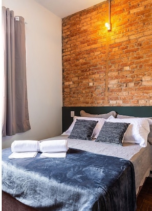 A hotel room with a brick wall, a bed with pillows, a blanket, and a towel on the bed. - Zest Teodoro (São Paulo)