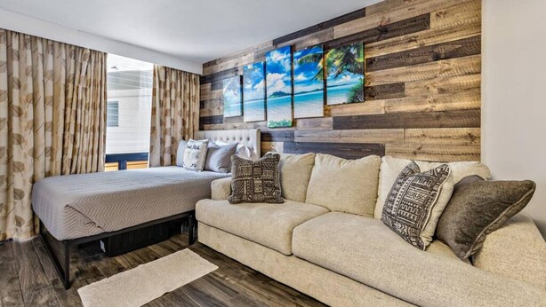 A bedroom with a bed, a sofa, and a wooden wall with paintings. - Inviting Waikiki Grand Hotel Room-1 Block to Beach (Honolulu)