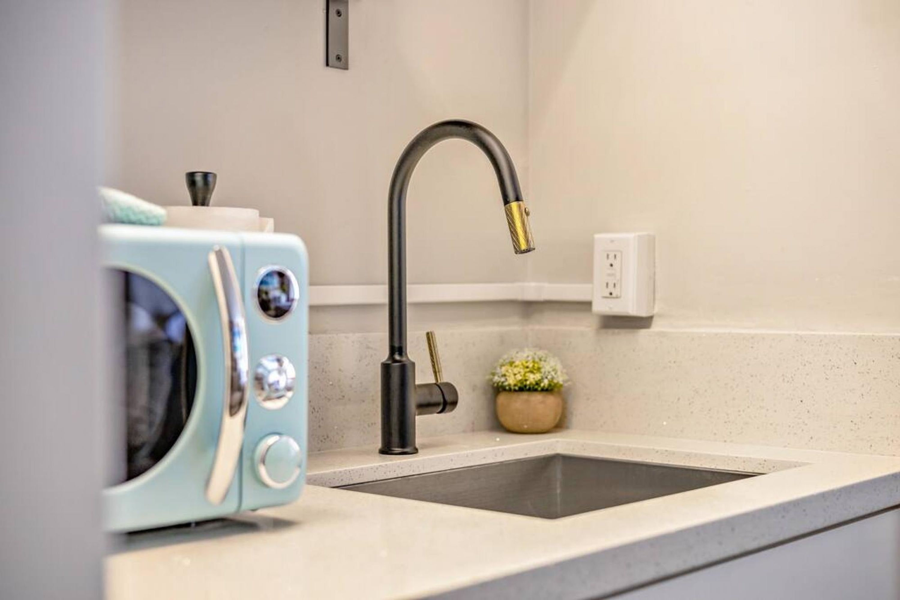 Una cocina con un grifo moderno, un microondas y una pequeña planta en maceta sobre la encimera.
