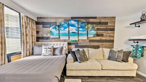 A bedroom with a bed, a sofa, and a wall with wooden panels and a beach scene painting. - Inviting Waikiki Grand Hotel Room-1 Block to Beach (Honolulu)