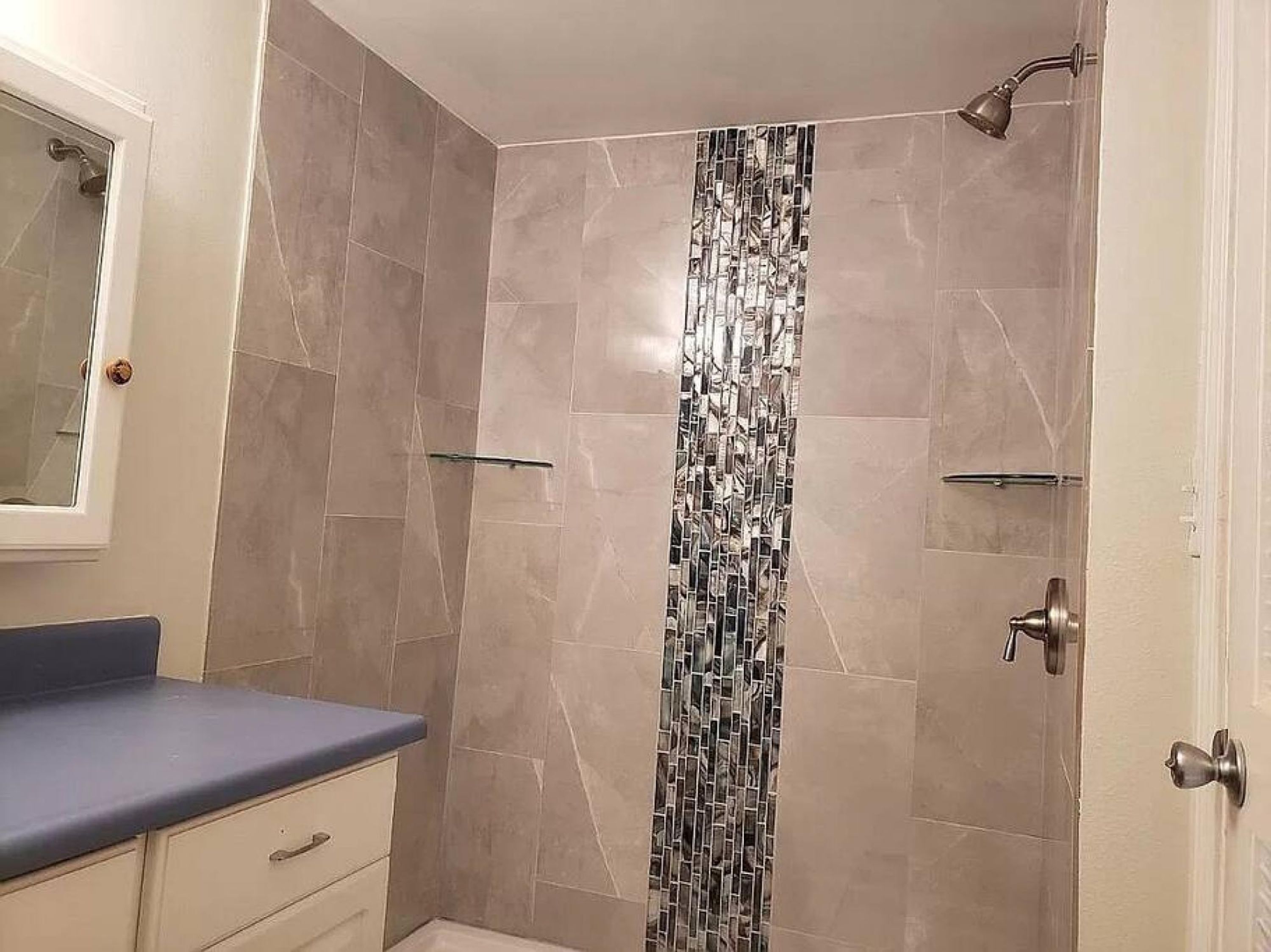 Un baño con ducha, espejo y tocador con encimera azul.