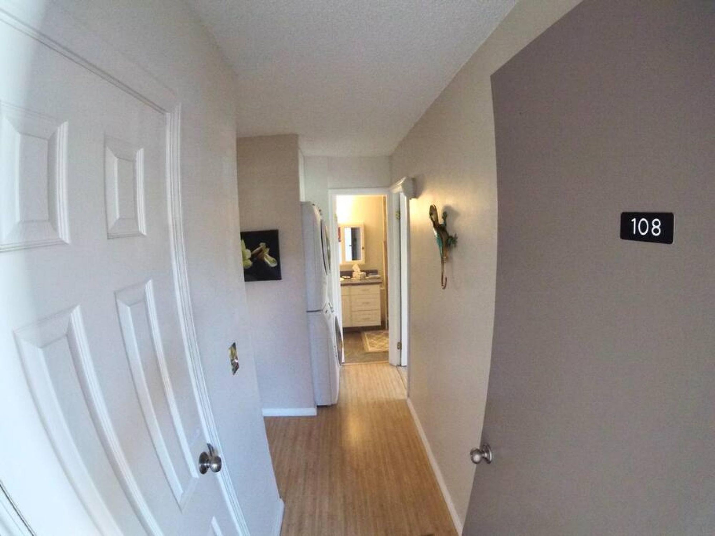 Un pasillo con una puerta marcada con el número 108, que da a una zona de cocina con refrigerador y microondas.