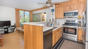 Una cocina moderna con gabinetes de madera, electrodomésticos de acero inoxidable, horno integrado, microondas y ventilador de techo.
