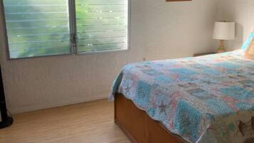 Un dormitorio con una cama de madera, una ventana con persianas, una lámpara de pared y un cuadro enmarcado.