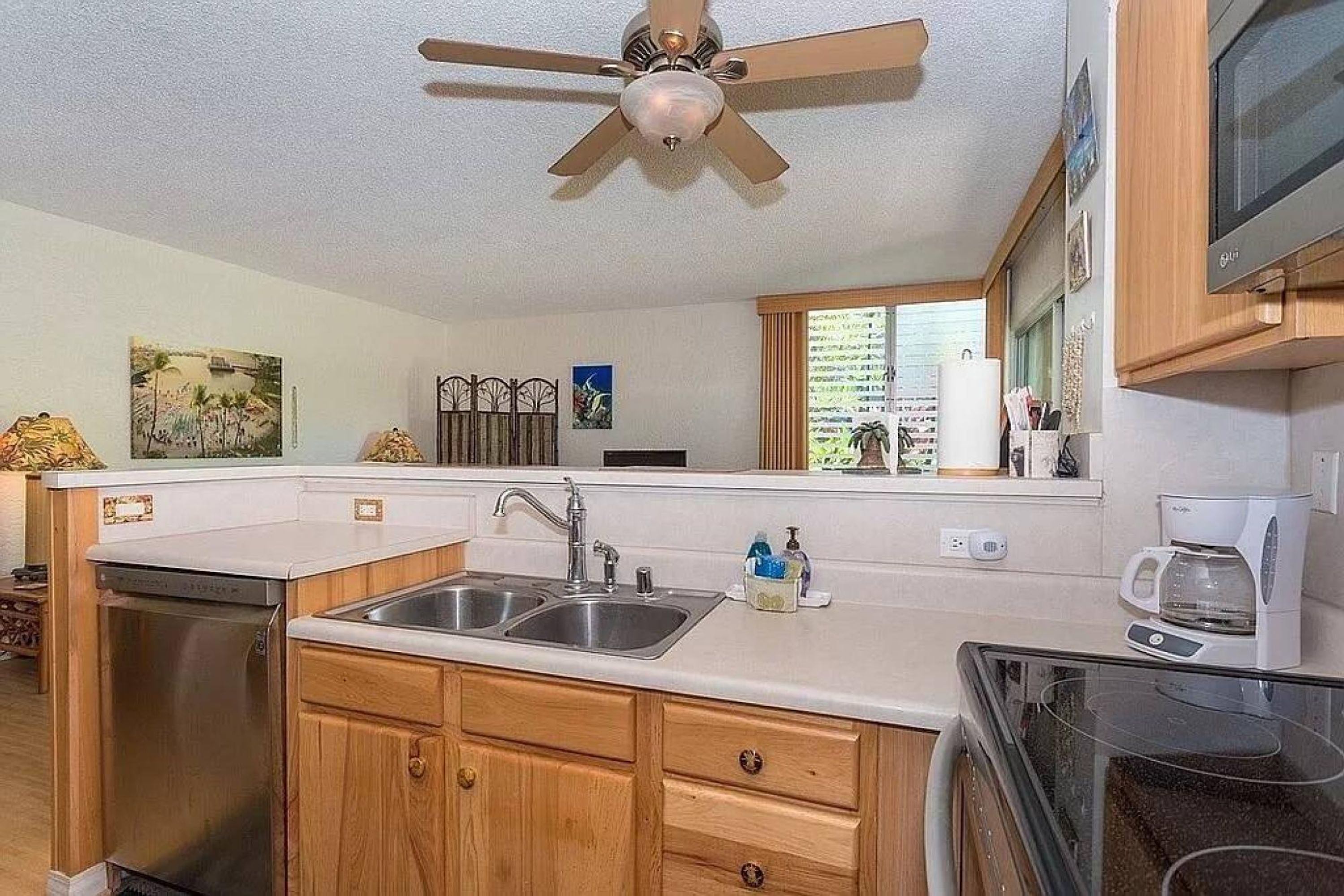 A kitchen with wooden cabinets, a double sink, a dishwasher, a ceiling fan, and a microwave.