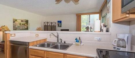 A kitchen with wooden cabinets, a double sink, a dishwasher, a ceiling fan, and a microwave.