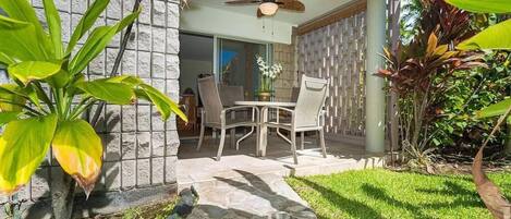 An outdoor patio with a table and chairs, surrounded by plants and a stone pathway.