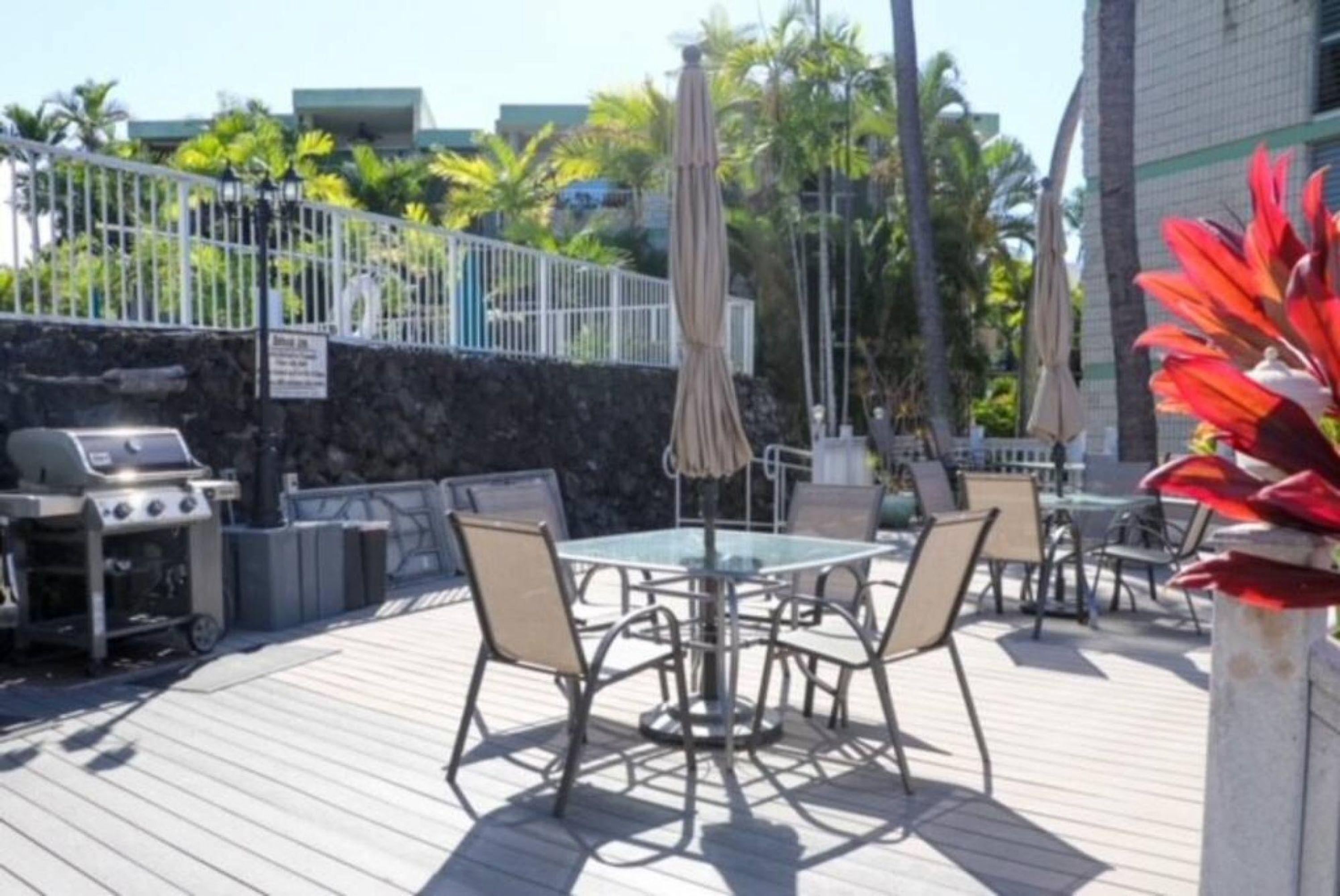 An outdoor patio with a round table and chairs, a grill, and umbrellas.