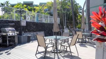 An outdoor patio with a round table and chairs, a grill, and umbrellas.