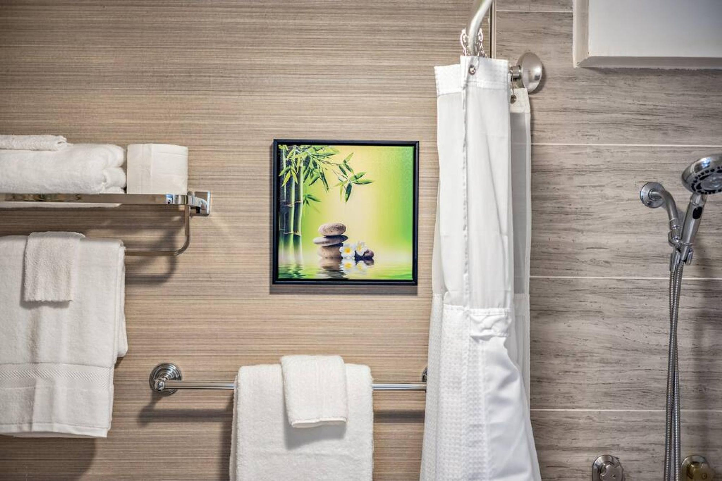 Casa de banho com parede de madeira, um quadro emoldurado com bambu, um porta-toalhas com toalhas, um chuveiro com chuveiro manual e um cortinado.