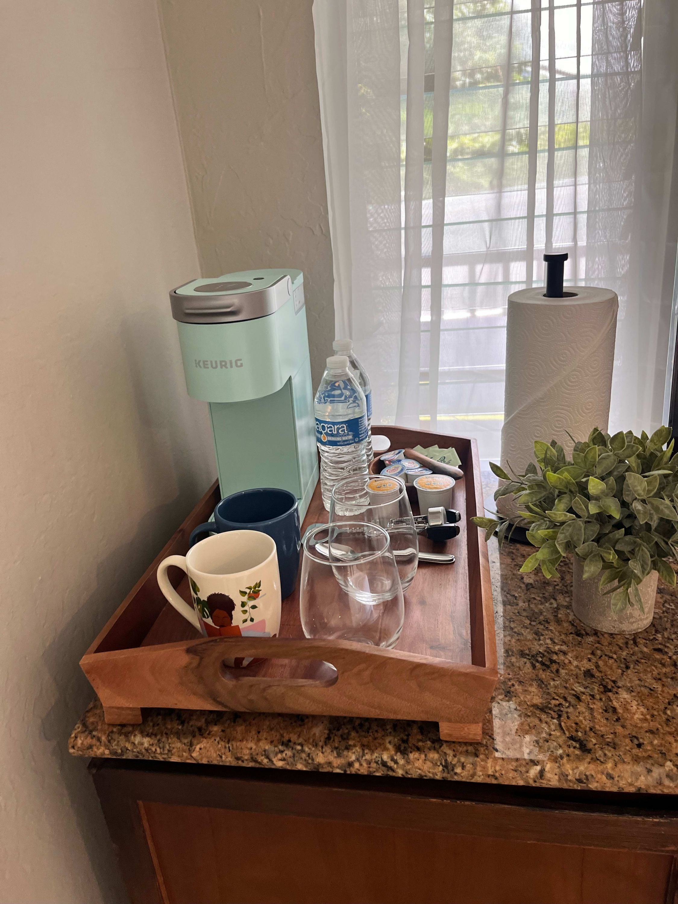 Una encimera de cocina con una cafetera, una botella de agua, una taza y una bandeja.