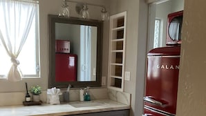 Un baño moderno con tocador, espejo y un electrodoméstico rojo, posiblemente un refrigerador.