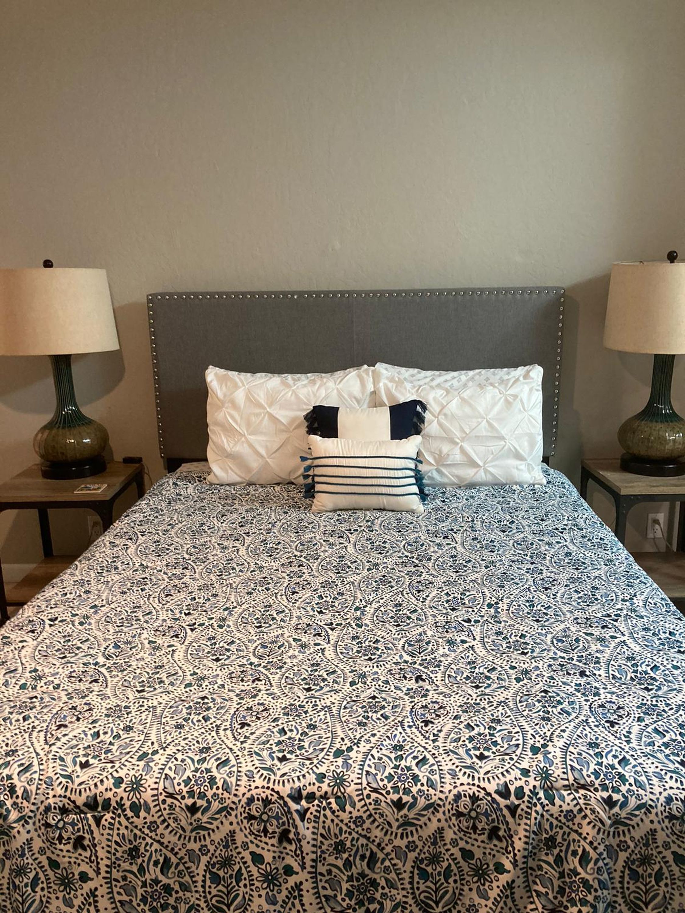 A neatly made bed with a patterned bedspread, two bedside lamps, and a headboard with a decorative border.
