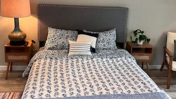 A bedroom with a bed, a lamp, a plant, and a ceiling fan.