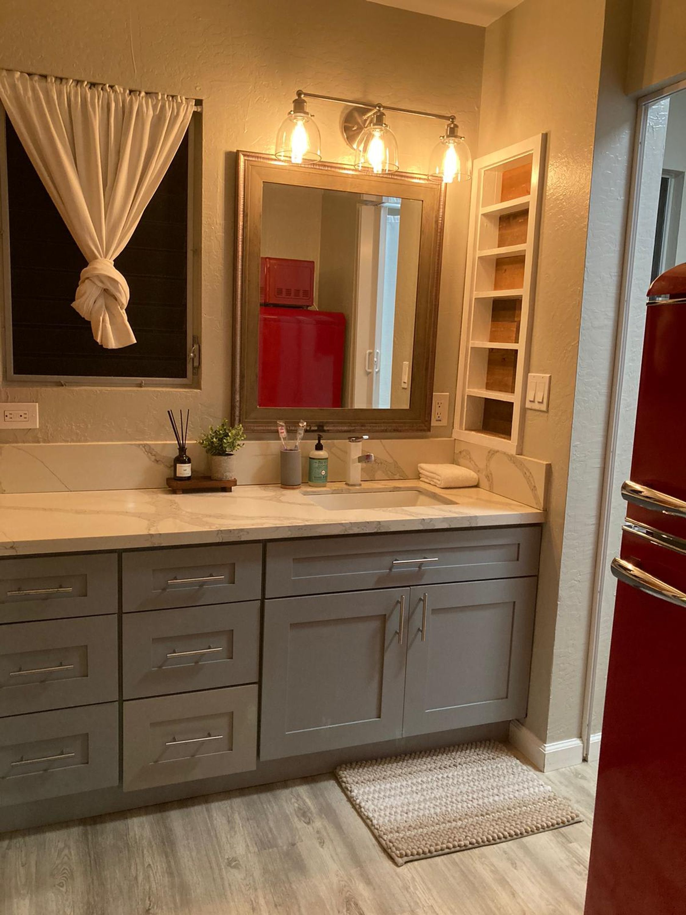 Un baño con un espejo grande, tocador con lavabo y un armario rojo.