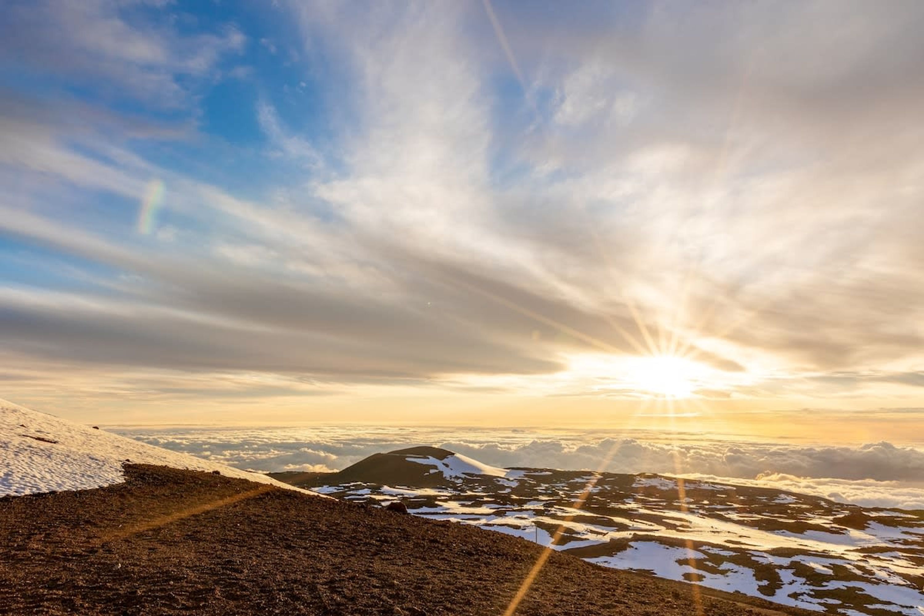 Paisaje montañoso con amanecer o atardecer, parches de nieve y cielo despejado.
