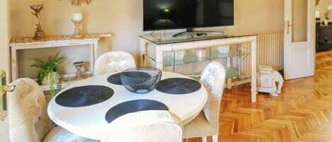 Cozy living room with a round dining table and comfortable seating for four, featuring a flat-screen TV and a stylish coffee table.