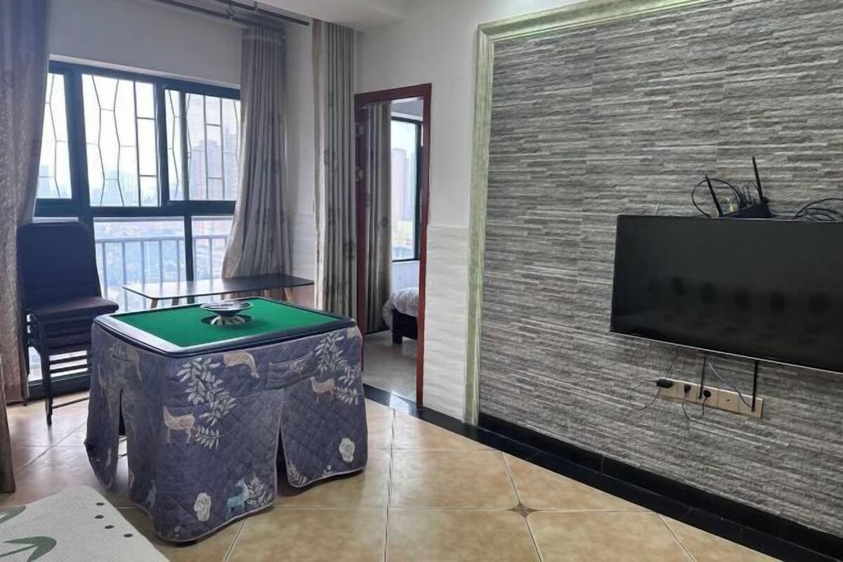 Une pièce avec une table de billard, un téléviseur fixé à un mur texturé et une vue par la fenêtre.